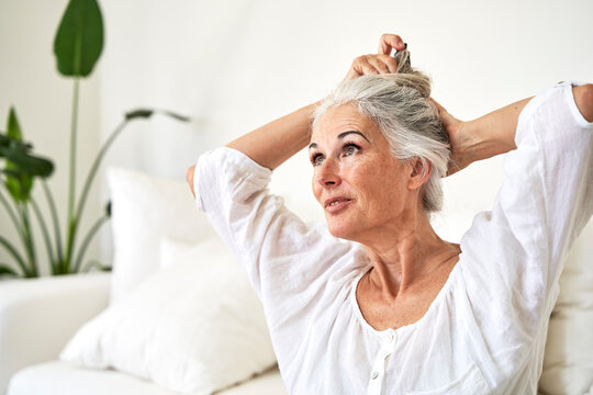 Mature Woman Tying Hair In Living Room