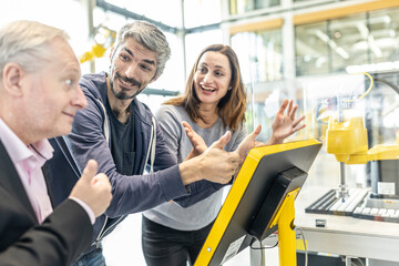 Happy colleagues giving thumbs up in robotic factory