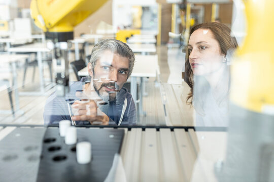 Engineers testing industrial robot in glass cabin