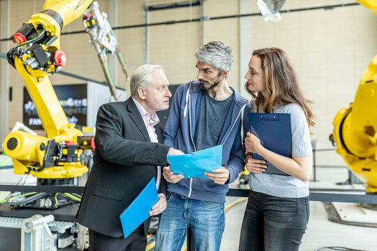 Manager discussing technical report with coworkers in front of industrial robot