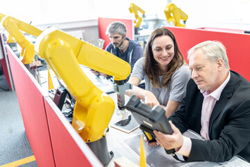 Senior engineer looking at digital control of female coworker at industrial robot