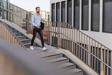 Young businessman with laptop bag walking downwards on staircase