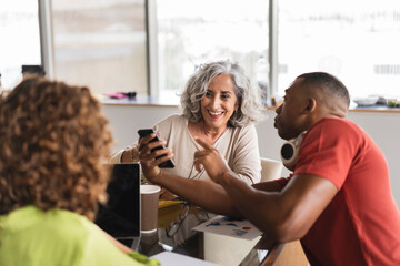 Businessman sharing mobile phone with senior businesswoman in office