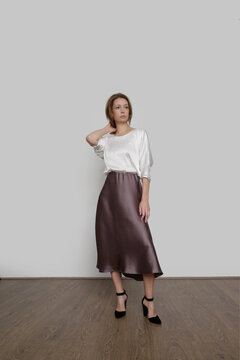 Series of studio photos of young female model wearing white silk satin batwing short sleeve blouse with mocha color midi skirt