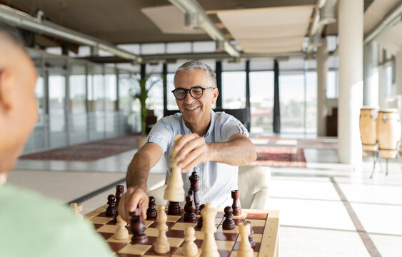 Smiling businessman wearing eyeglasses playing chess with colleague in office