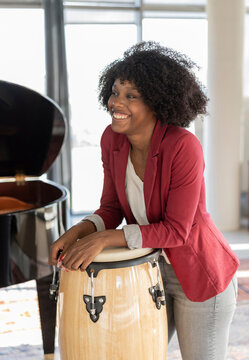 Happy businesswoman with Afro hairstyle leaning on conga drum in office