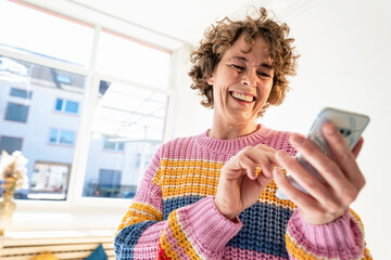 Happy mature woman text messaging through smart phone at home