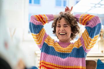 Happy woman sitting with hands behind head at home