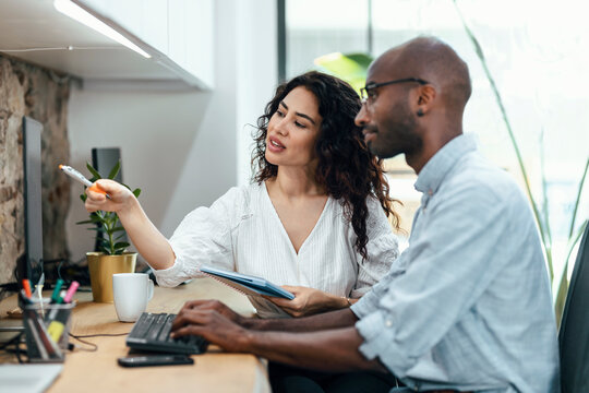 Businesswoman pointing at computer monitor sitting by businessman at office