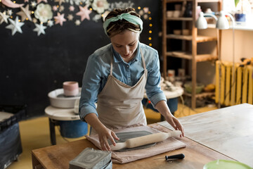 Smiling craftsperson rolling clay with pin on workbench at art studio