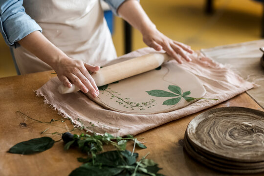 Hands of craftsperson rolling leave on clay with pin at art studio