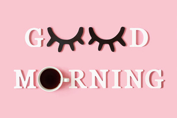 Creative good morning concept. White letters, black eyeleshes and alarm clock on pink background....