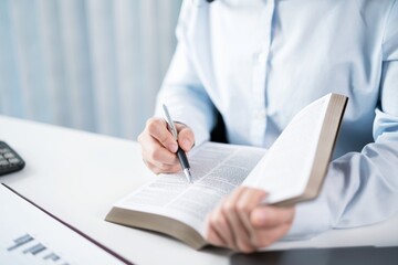 Portrait of  Asian Business woman working from office taking reading and writing notes in note pad working on laptop computer  in her workstation
