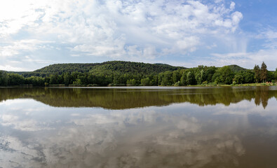 Panorama of a lake in the morning with a forest and a blue cloudy sky