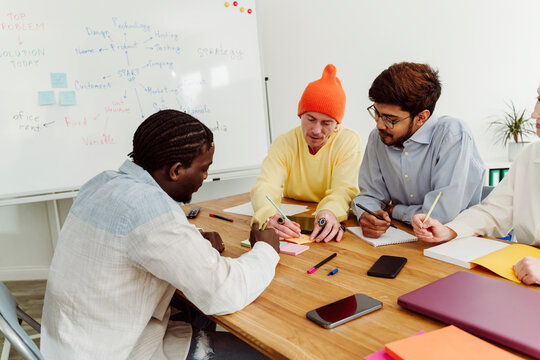 Businessman showing adhesive note to colleagues at desk in office