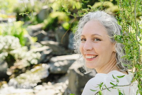 Happy woman with gray hair by plants on sunny day