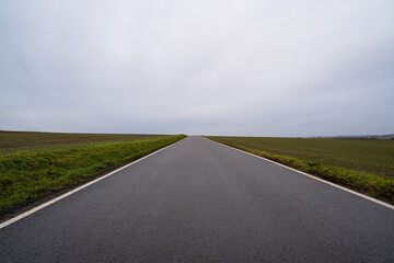 Asphalt country road between agricultural fields with a cloudy sky in autumn