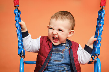 Screaming toddler baby boy rides on a swing. A frightened child swings on the playground, kid aged one year