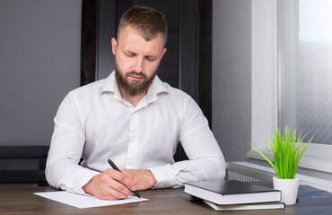 Naklejka premium Young businessman is sitting at the table. A man in a shirt. Office worker. A man with a beard.
