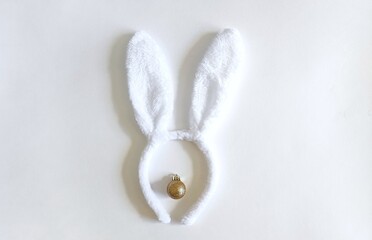 Obraz premium white rabbit ears and a golden Christmas ball on a white background, a symbol of the New Year of the rabbit 2023, the concept of Merry Christmas and holiday, Christmas rabbit ears copy, space