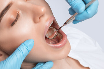 A dentist doctor treats caries on a tooth of a young beautiful woman in a dental clinic. Tooth...