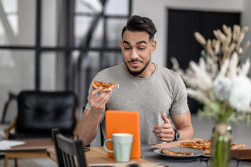 Man eating pizza looking in surprise at tablet