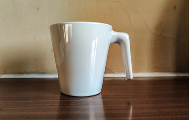 A white coffee mug is placed on a wooden table near a light brown wall.