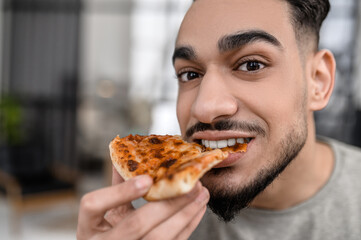 Face of man looking at camera biting pizza