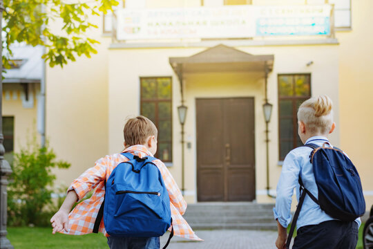 children running to school with backpacks on sunny day. Begining of academic year. Boys by school doorstep