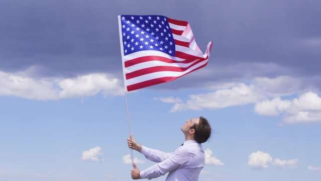 Young man waving the flag of the United States of America.
 The flag of the United States of America is waving in the wind. Patriotism, Country, Victory, Celebration, victory day, liberation, independ