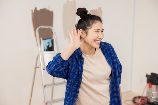 Girl of Asian appearance with beautiful smile shows with right hand that she is listening to something. In background repairs are taking place and everything needed for this is standing.