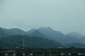 Nearby are the rooftops of buildings, and in the distance are the mountains entwined with mist. View of the mountains in the mist