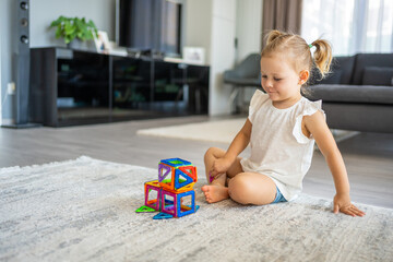 Little girl playing colorful magnet plastic blocks kit at home. The child playing educational...