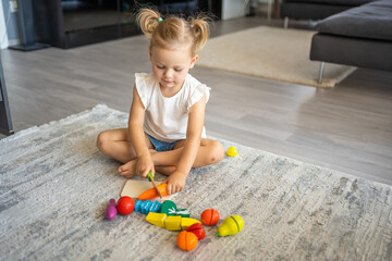Cute little toddler girl playing at home with eco wooden toys. Happy child cutting vegetables and...