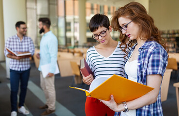 Happy university students studying with books in library. Group of multiracial people in college