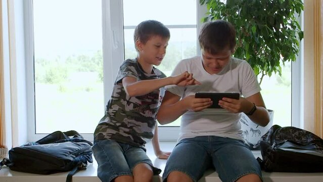 Caucasian schoolboys they use a tablet computer and watch videos, play games with a smile on their face. Two brothers watch interesting videos together on tablet or smartphone. They laugh and indulge