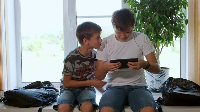 Caucasian schoolboys they use a tablet computer and watch videos, play games with a smile on their face. Two brothers watch interesting videos together on tablet or smartphone. They laugh and indulge
