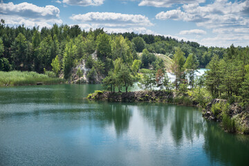 Fototapeta na wymiar A rocky, tree-covered island in a blue-green lake where there was a granite quarry