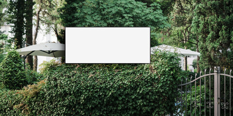 Blank sign board fixed against green bushes near hotel entrance outdoor
