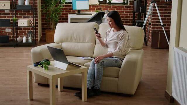 Excited woman reading work email about job promotion while working remotely from home. Cheerful young adult person getting notified on mobile about salary raise while sitting on sofa.