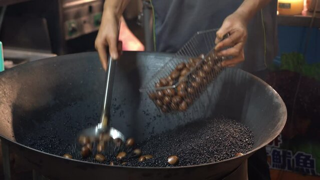 Close up shot of famous Taiwan night market, close up shot of professional, roasting chestnuts in sand with brown sugar in high heat with aromatic smokes.