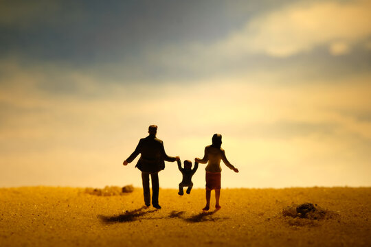 Miniature people toy figure photography. Couple with one child son daughter walking on sand beach at dawn. Family outing day concept