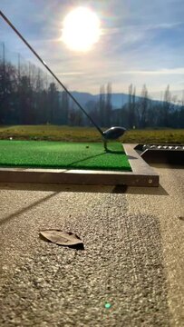 Golfer Hitting the Golf Ball with Driver on Mat in Driving Range with Sunlight in Switzerland.