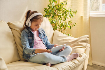 Cute little girl in casual clothes and headphones using a tablet