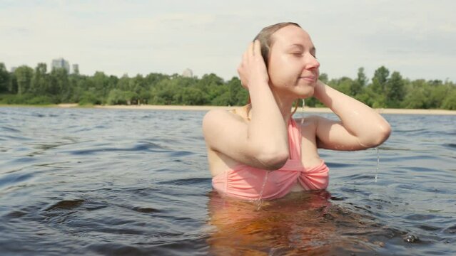 A young blonde women in a pink swimsuit dives into the water at the river. Swimming woman in summer on nature.Portrait of a wet woman