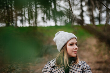 Portrait of young woman in coat and knitted cap in autumn nature, walking in forest.