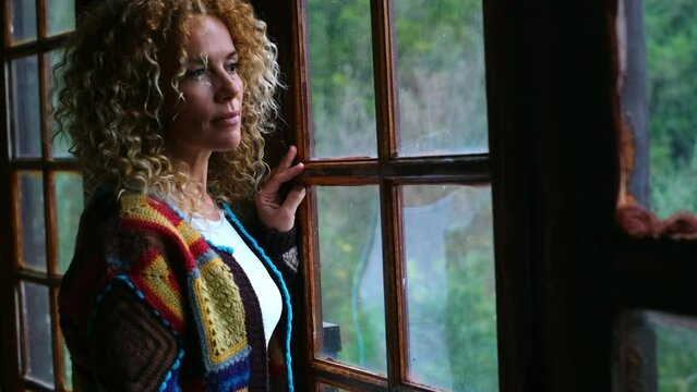 Thoughtful woman smile and look outside the window in home leisure indoor activity. Female dreaming future life and enjoy wooden chalet apartment. Pretty lady people with curly hair in autumn