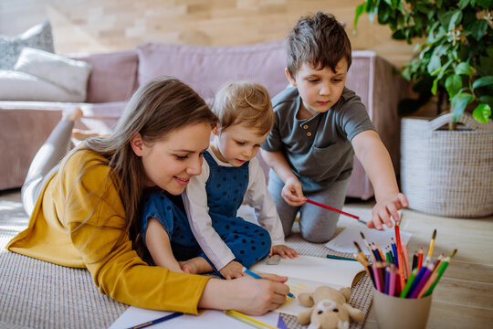 Happy mother with her little children at home drawing together.