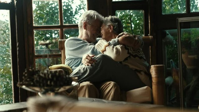Happy old senior couple kiss and enjoy love and relationship together sitting on a sofa in home wooden chalet. Mature and retired man and woman in romantic leisure activity having fun indoor