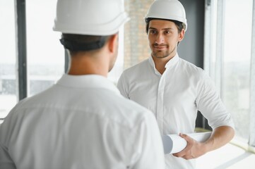 A front view of two smart architects with white helmets reviewing blueprints at a construction site on a bright sunny day